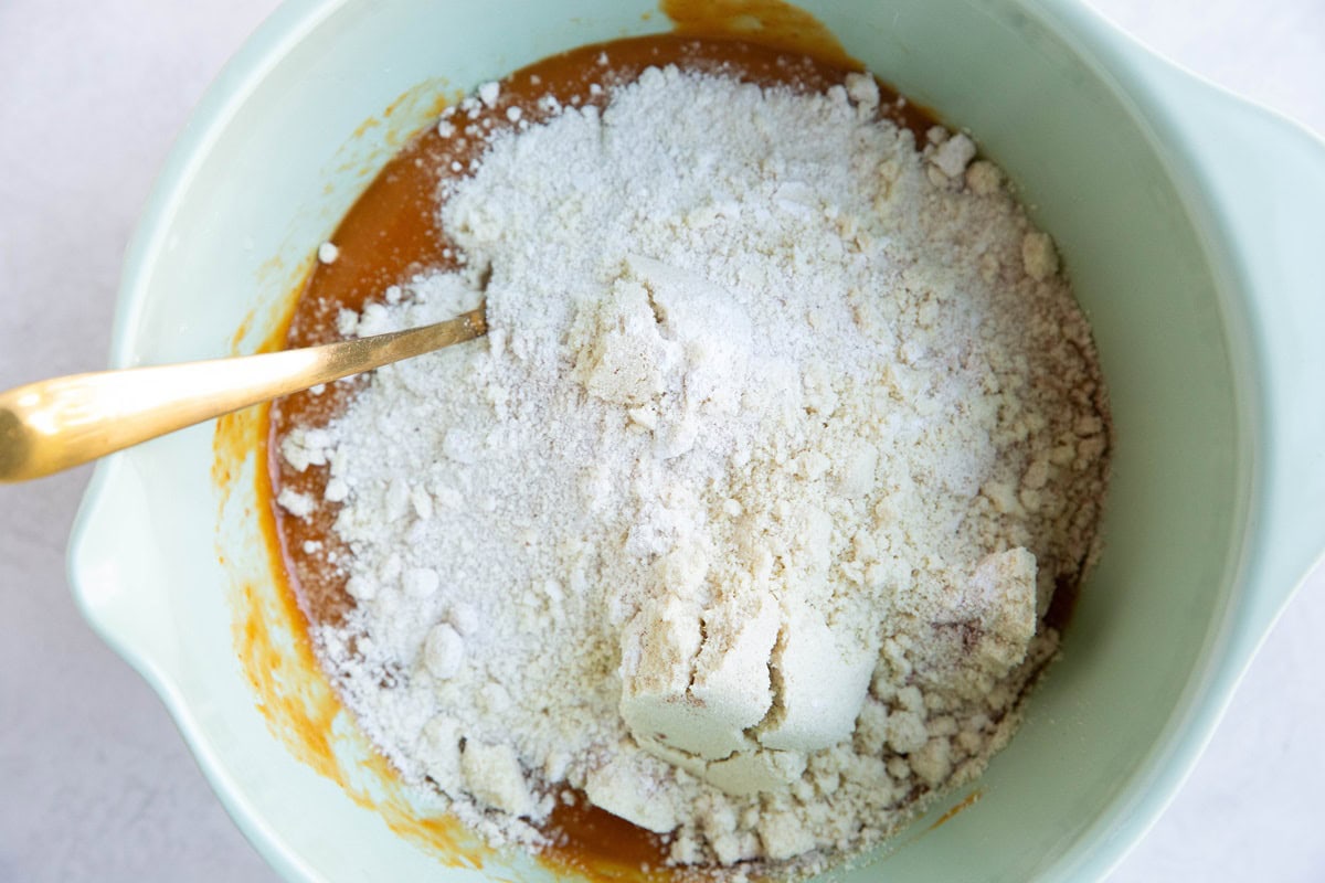 Dry ingredients on top of wet ingredients in green mixing bowl to make pumpkin muffins.