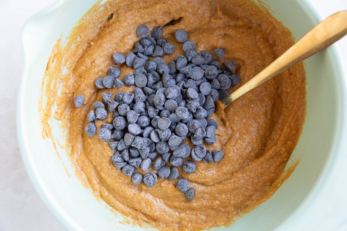 Pumpkin muffin batter in a large bowl with chocolate chips on top, ready to be mixed in.