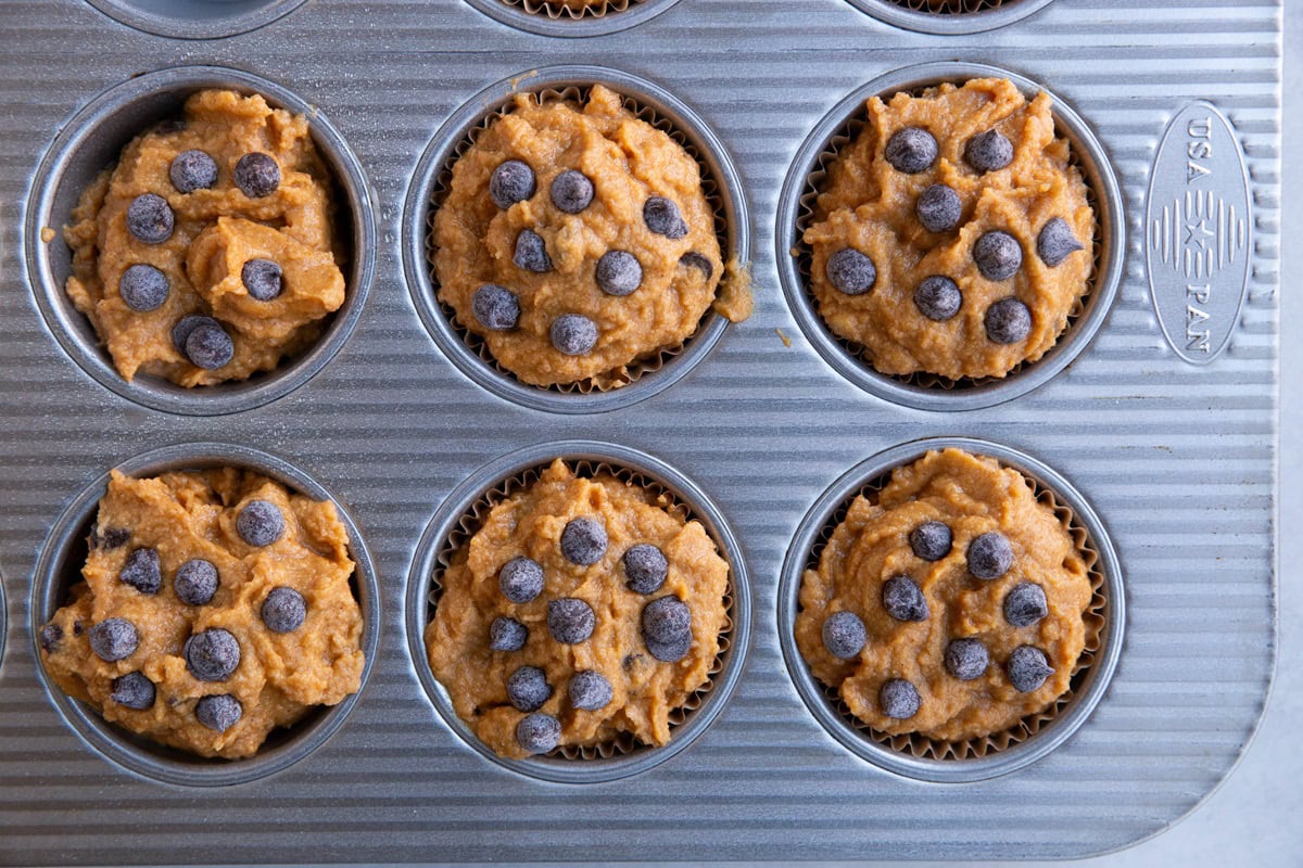 Pumpkin muffin batter in a muffin tray with chocolate chips sprinkled on top.