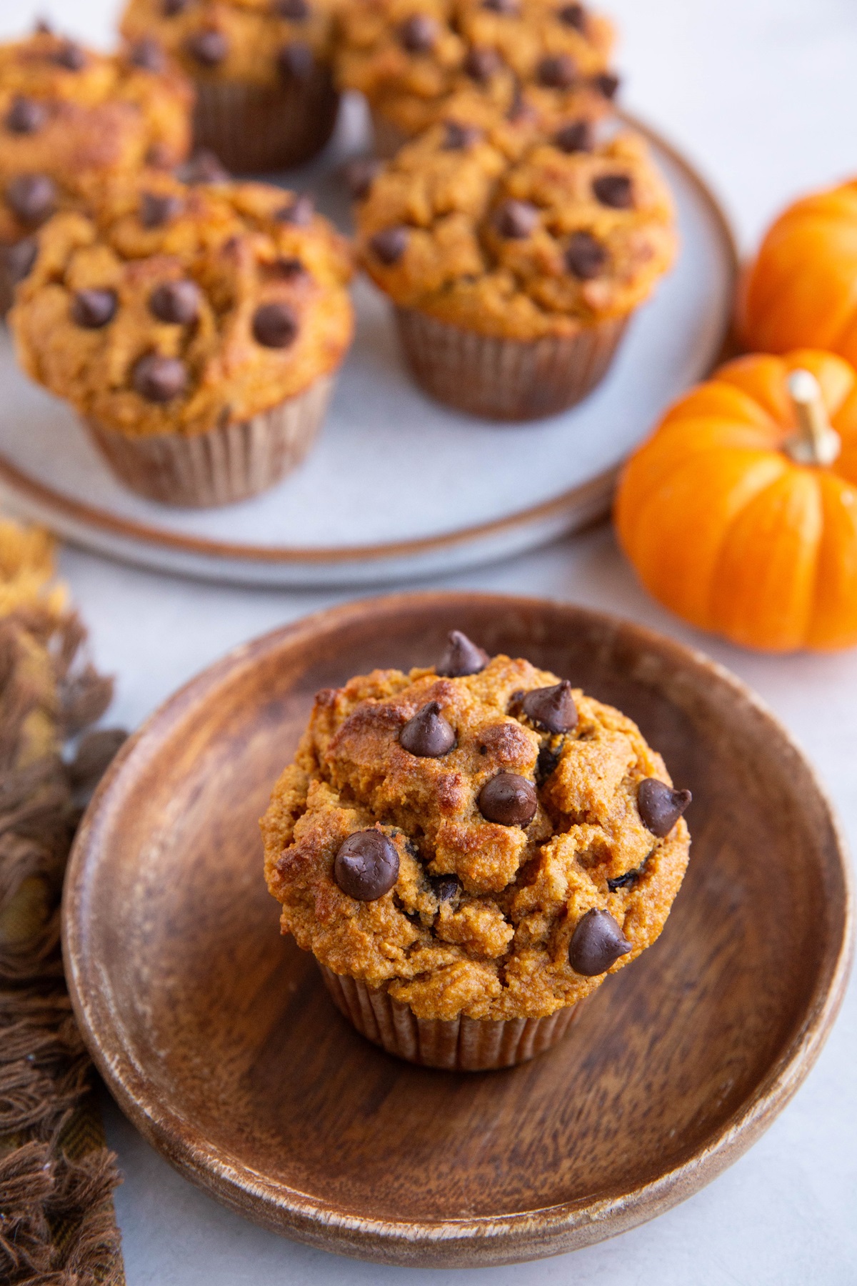 Pumpkin muffin on a wooden plate with a plate of more muffins in the background.