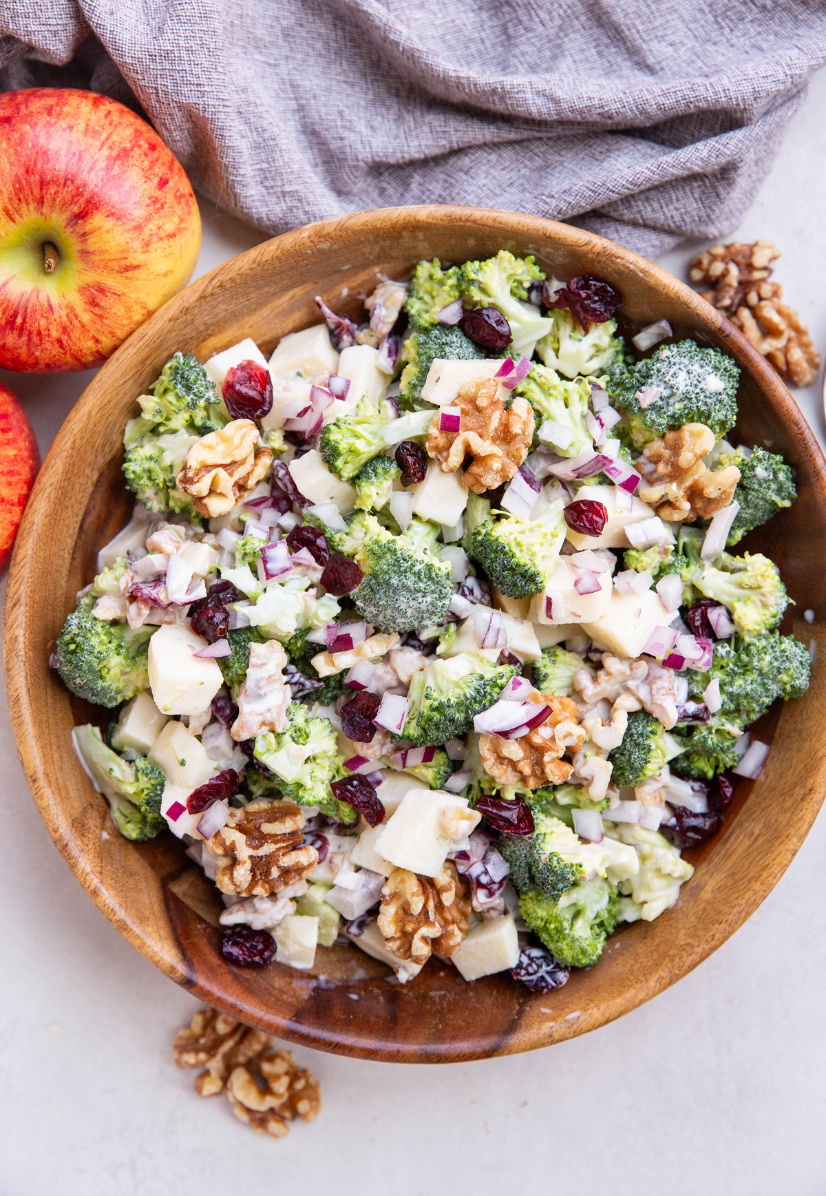 Wooden bowl full of apple broccoli salad with apples and a napkin to the side.