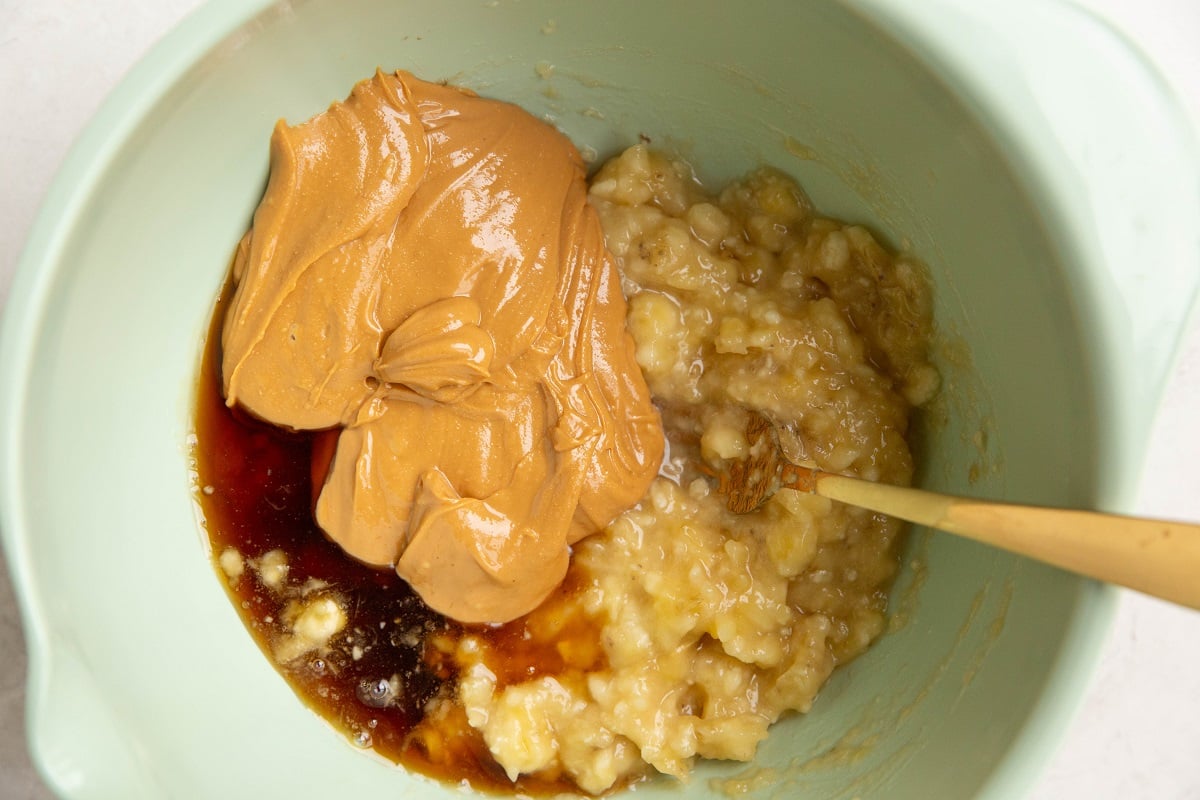 Mashed bananas, peanut butter, and pure maple syrup in a mixing bowl, ready to be mixed together.