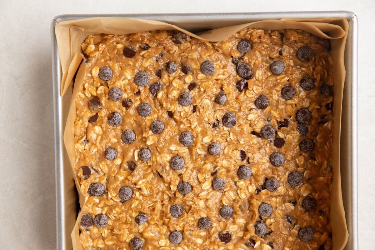 Parchment-lined baking pan with peanut butter oatmeal mixture inside, ready to be baked.