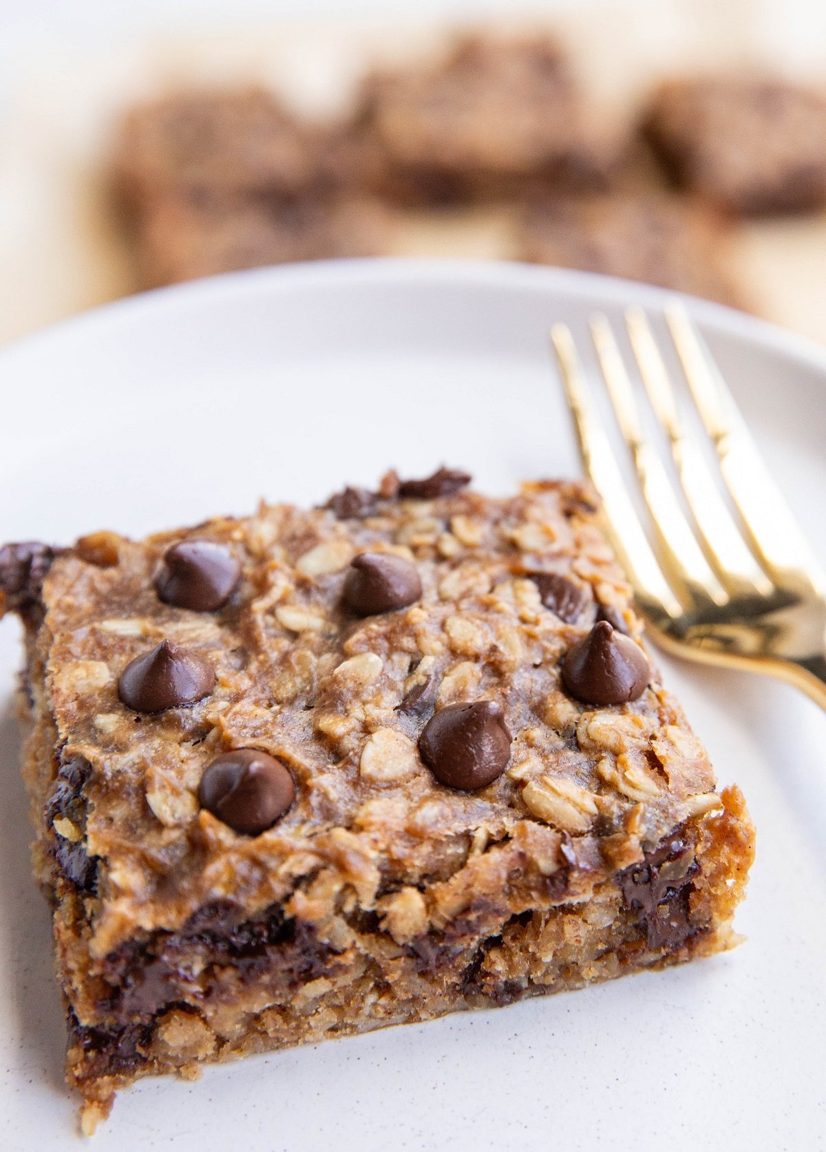 Slice of banana peanut butter oatmeal bar on a plate with a fork and more bars in the background.
