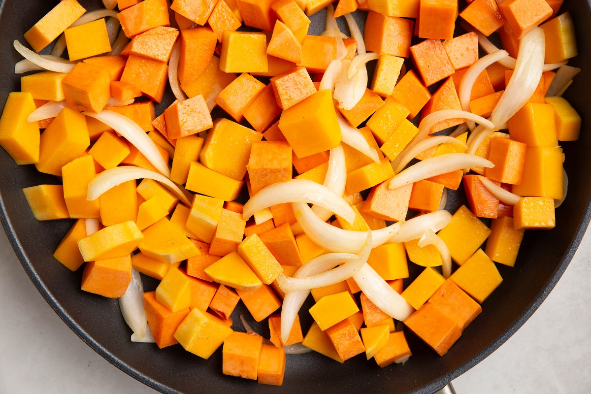 Chopped butternut squash, onion, and yams cooking in a skillet.