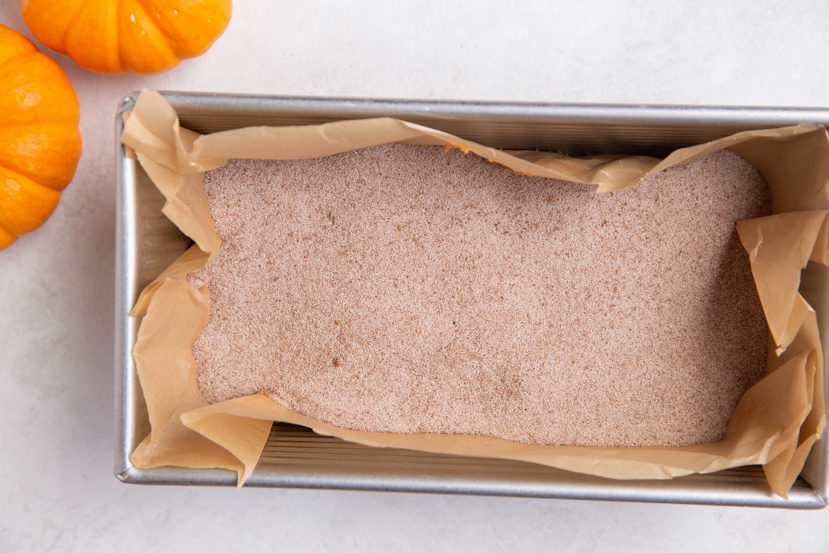 Loaf pan with pumpkin bread batter in a loaf pan with cinnamon and sugar sprinkled on top.