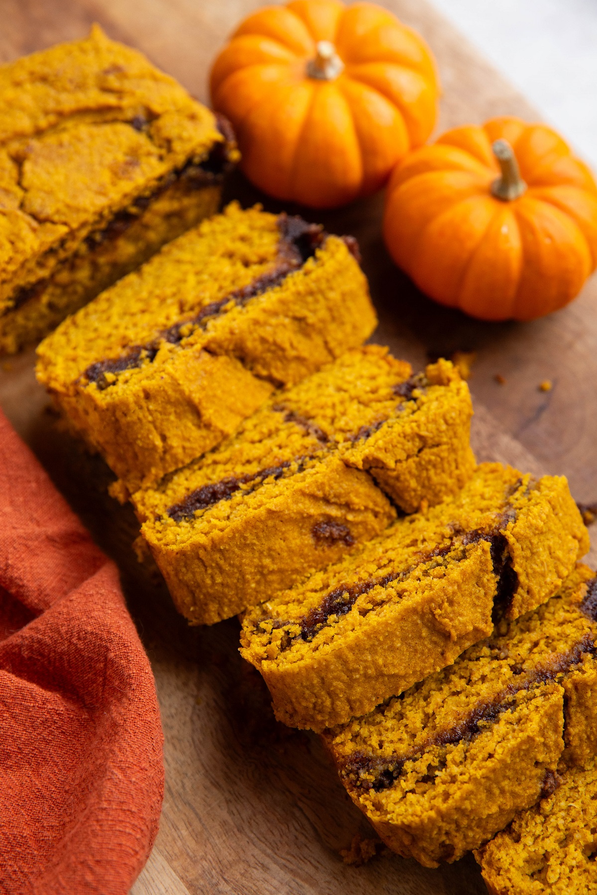 Loaf of pumpkin bread on a cutting board cut into slices with small pumpkins in the background.