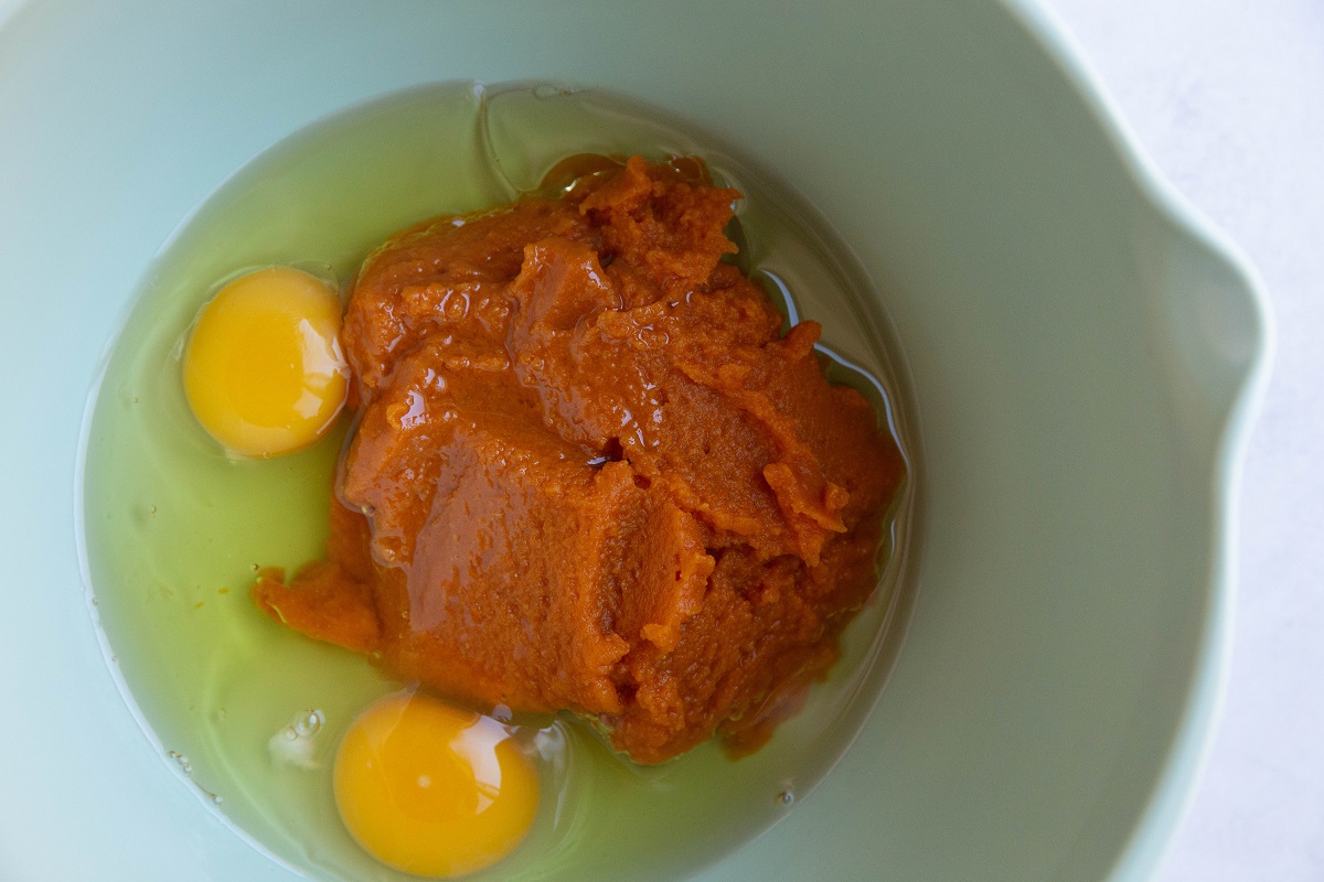 Pumpkin puree, eggs, and oil in a green mixing bowl to make pumpkin bread.