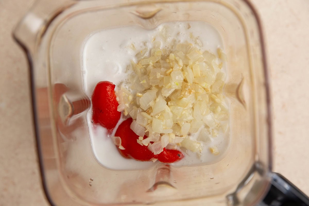 Blender with coconut milk, onion, garlic, and roasted red peppers.