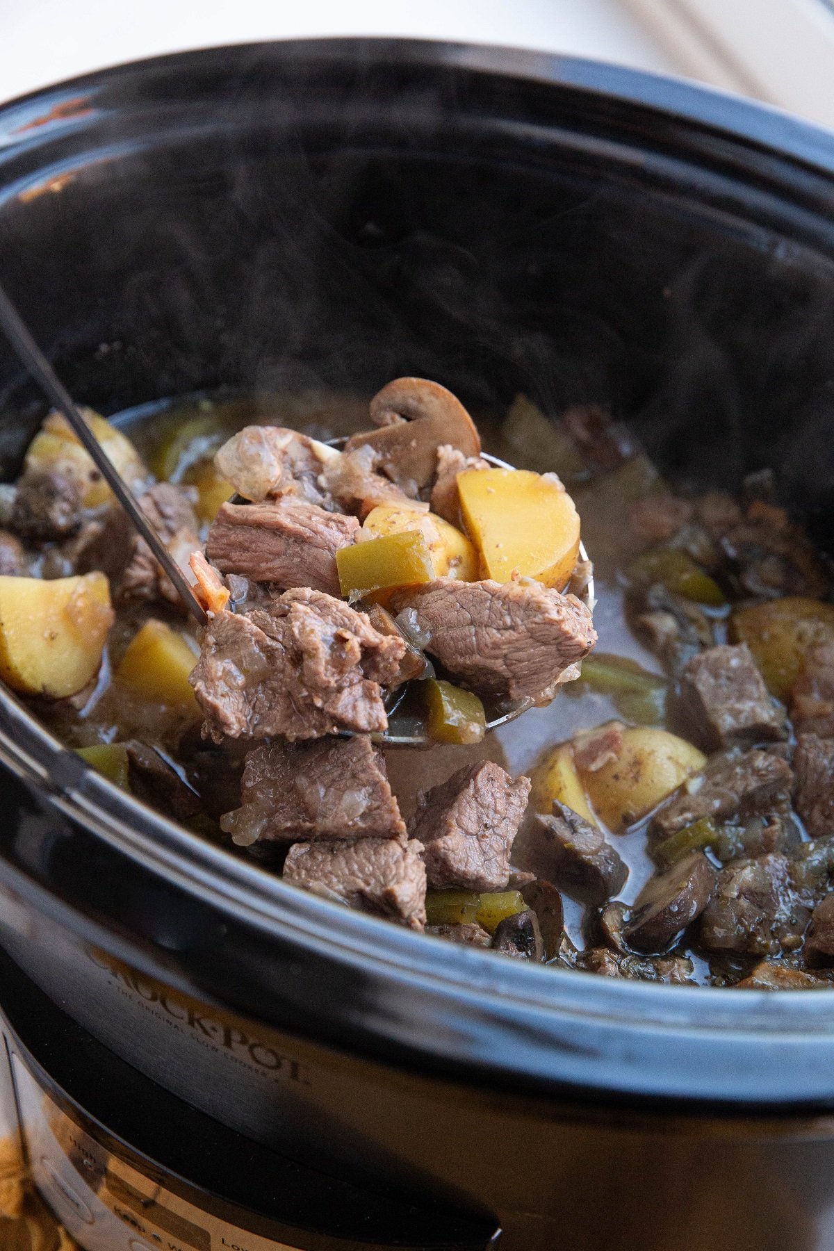 Crock pot full of steak and potato soup with a ladle scooping some of the soup out to serve.