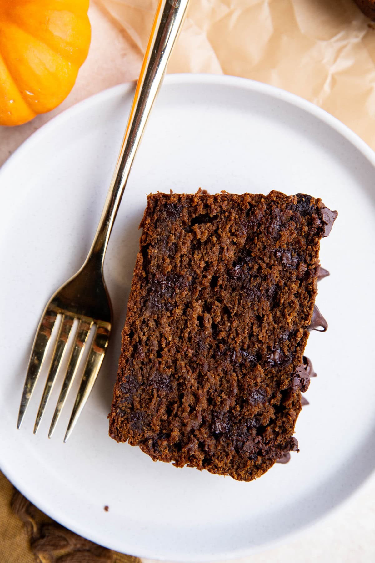 Slice of chocolate pumpkin bread on a white plate with a gold fork, ready to eat.