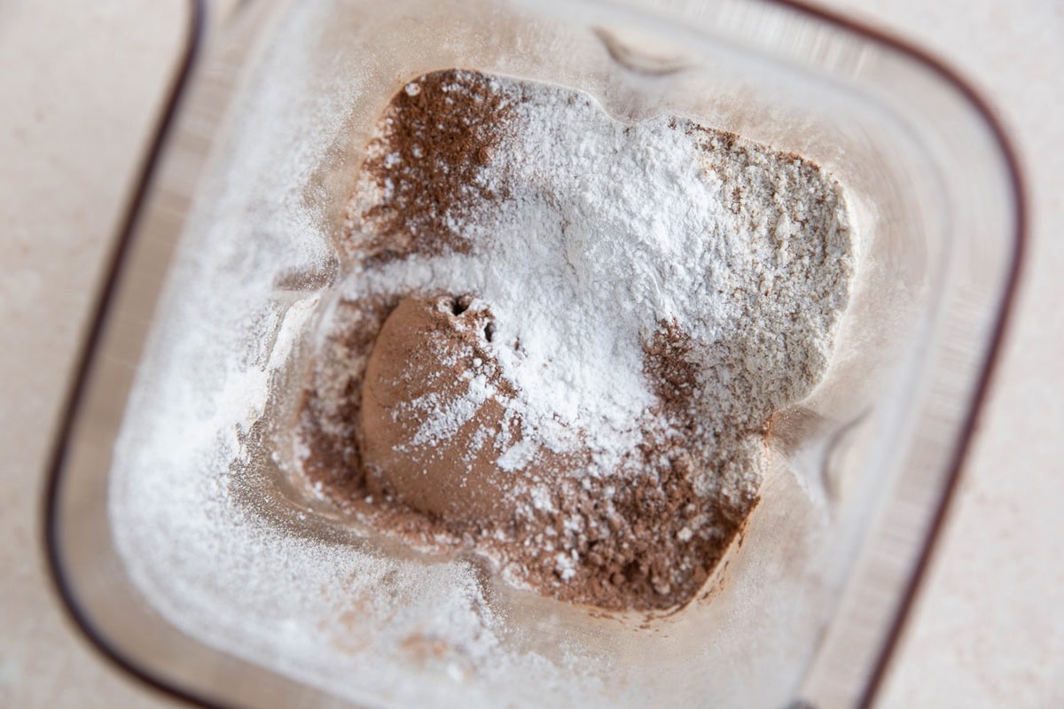 Oat flour, cocoa powder, baking powder, pumpkin spice and salt in a blender, ready to be blended.