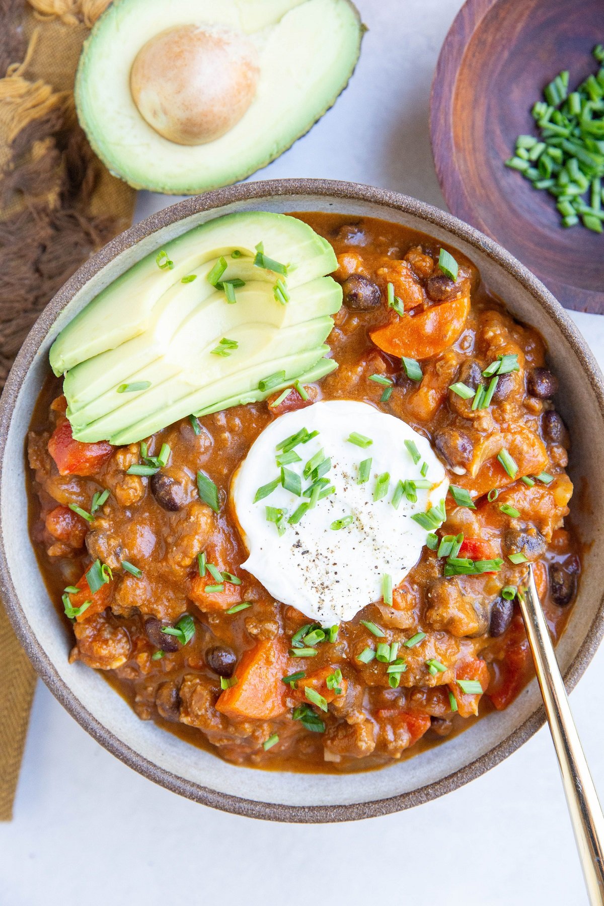 Bowl of beef pumpkin chili with sour cream, chives, and avocado on top.