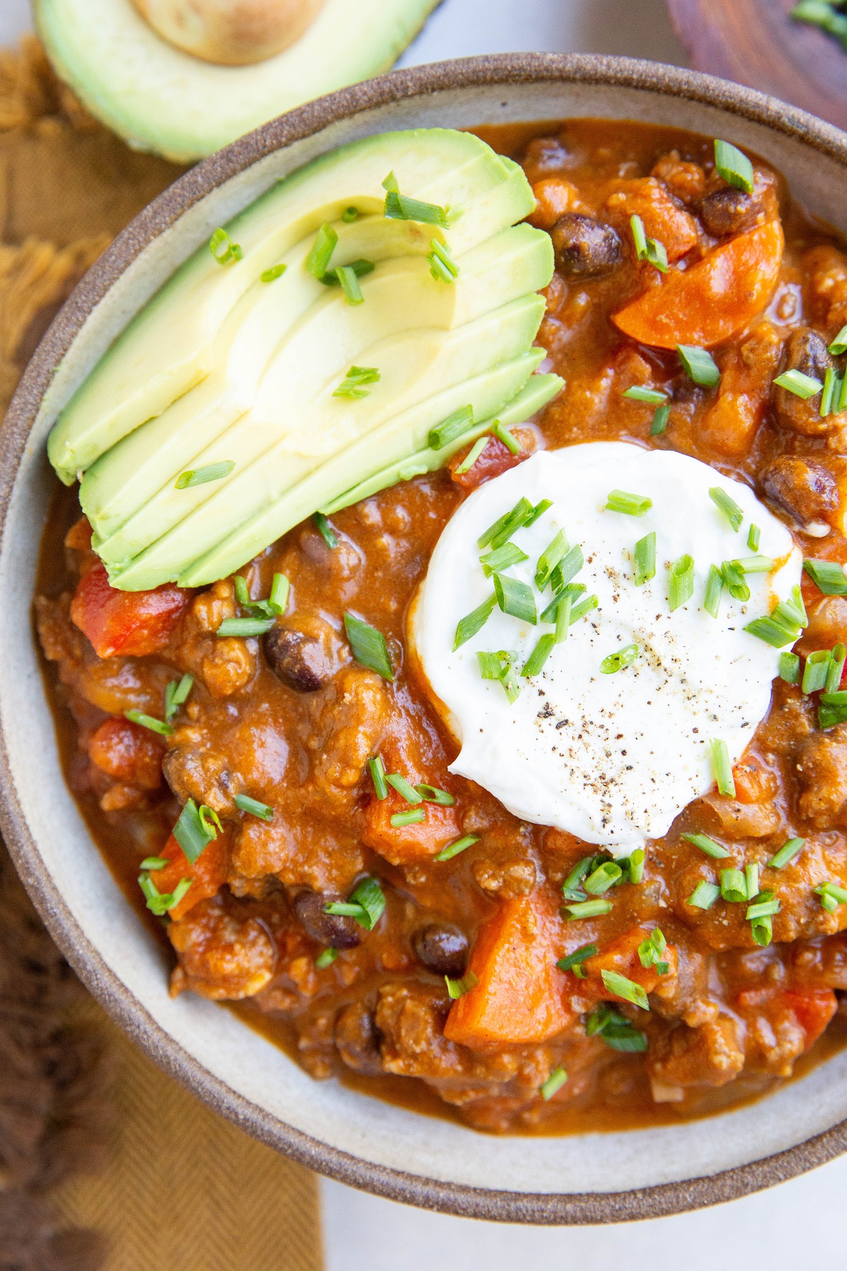 Large bowl of pumpkin chili with sliced avocado, chopped chives, and sour cream on top.