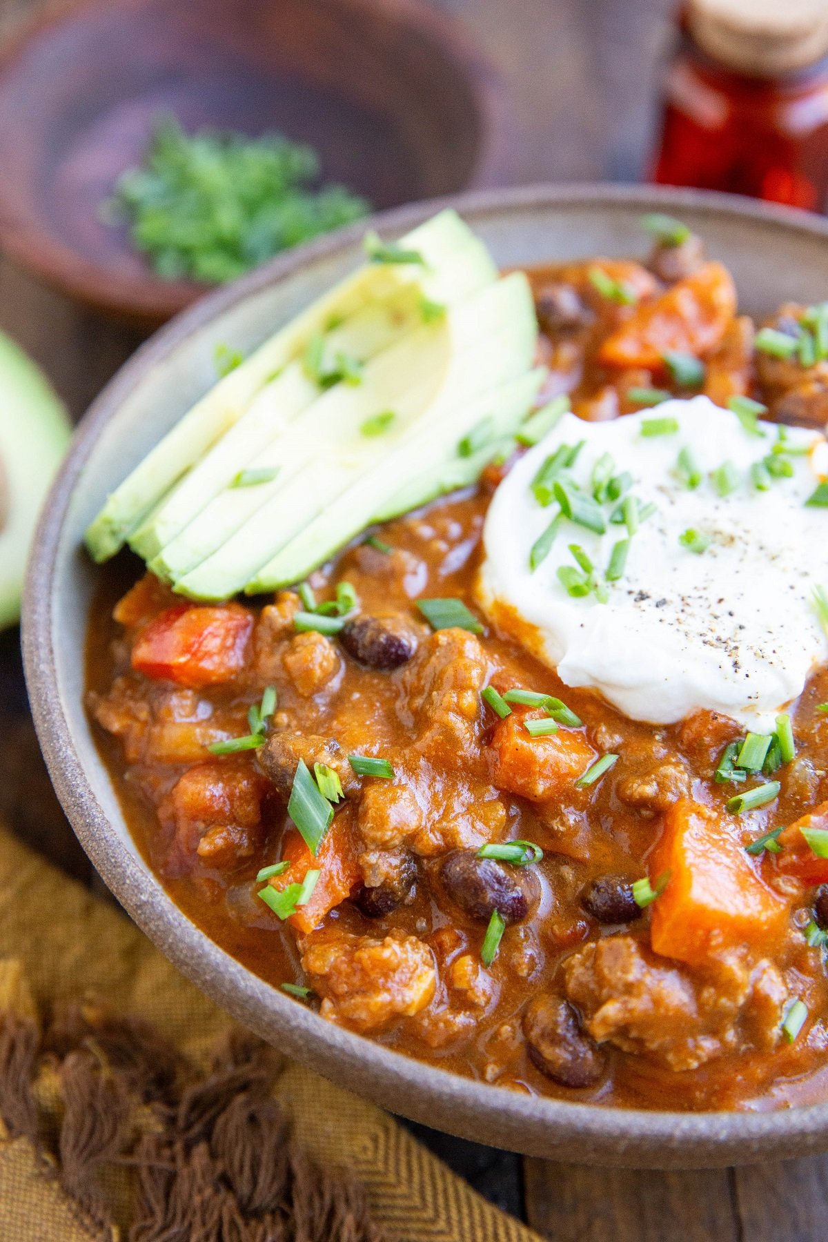 Close up bowl of pumpkin beef chili with chili toppings on top.