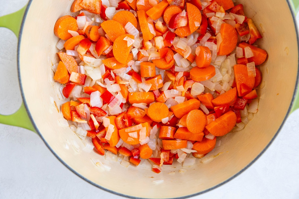 Onion, carrots, and bell peppers cooking in a large pot.