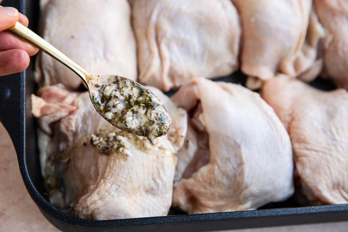 Hand spooning garlic butter herb mixture over the chicken thighs.