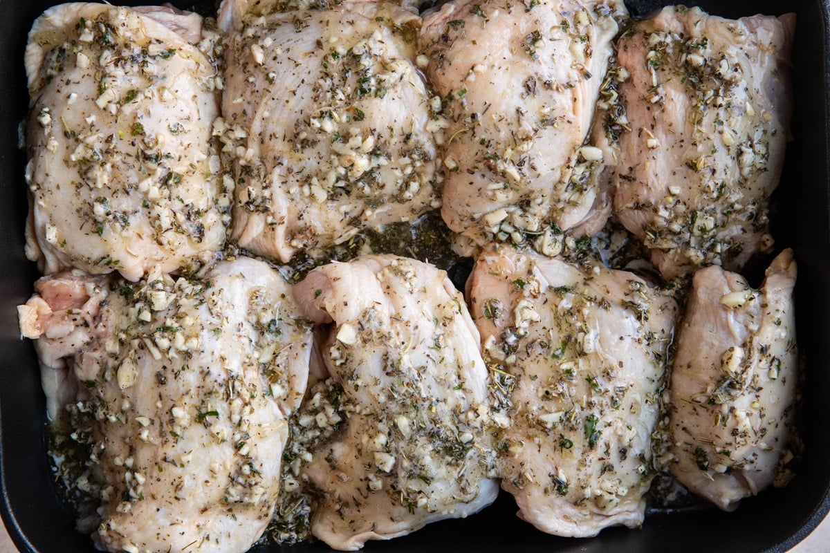Raw chicken thighs covered with garlic butter herb sauce in a large casserole dish, ready to go into the oven.