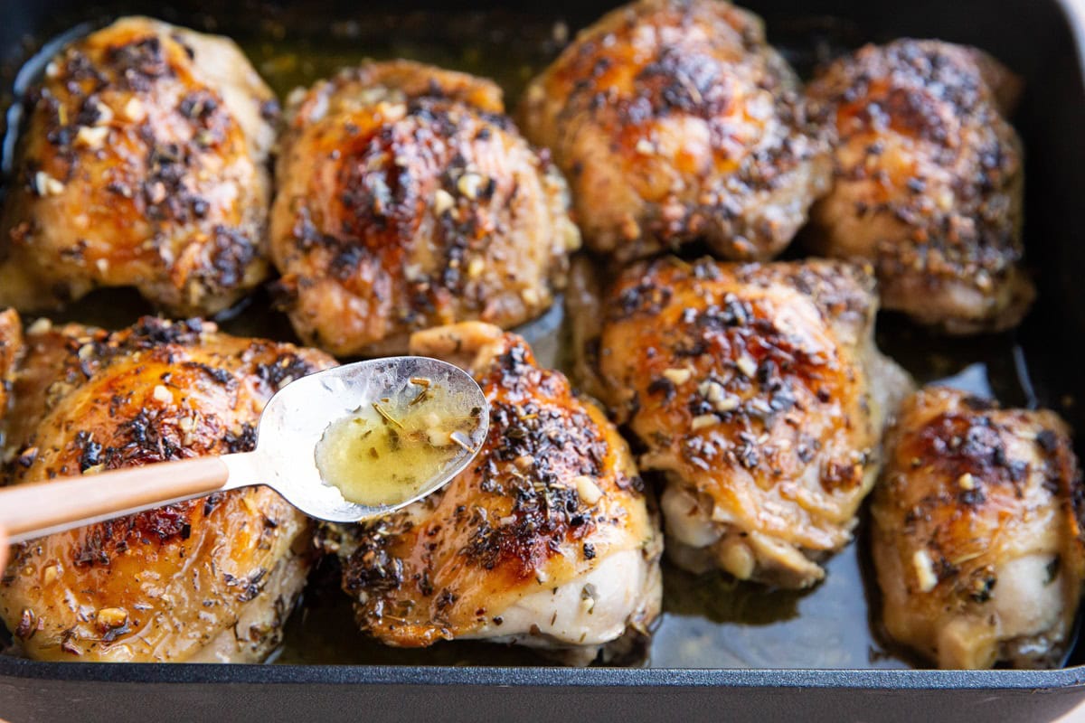 Spoon basting chicken thighs with juices from the pan.