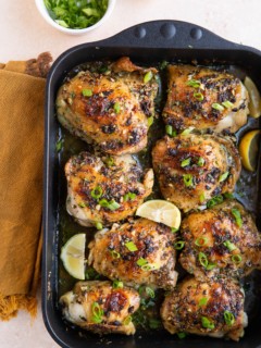 Finished garlic butter chicken thighs in a large roasting pan with chopped green onions and half a lemon to the side.