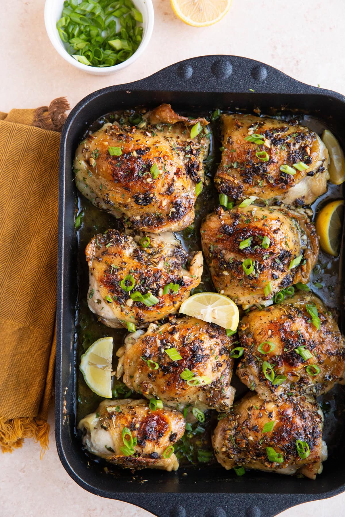 Finished garlic butter chicken thighs in a large roasting pan with chopped green onions and half a lemon to the side.