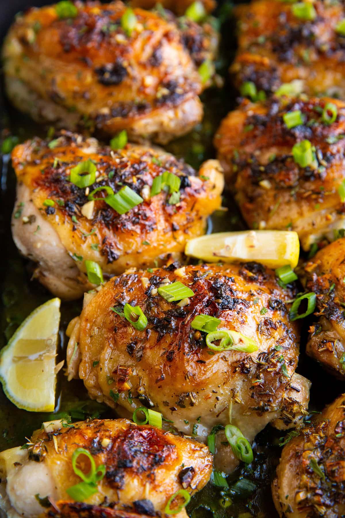 Garlic Butter Baked Chicken Thighs in a casserole dish with chopped green onions on top and lemon slices. Ready to serve.