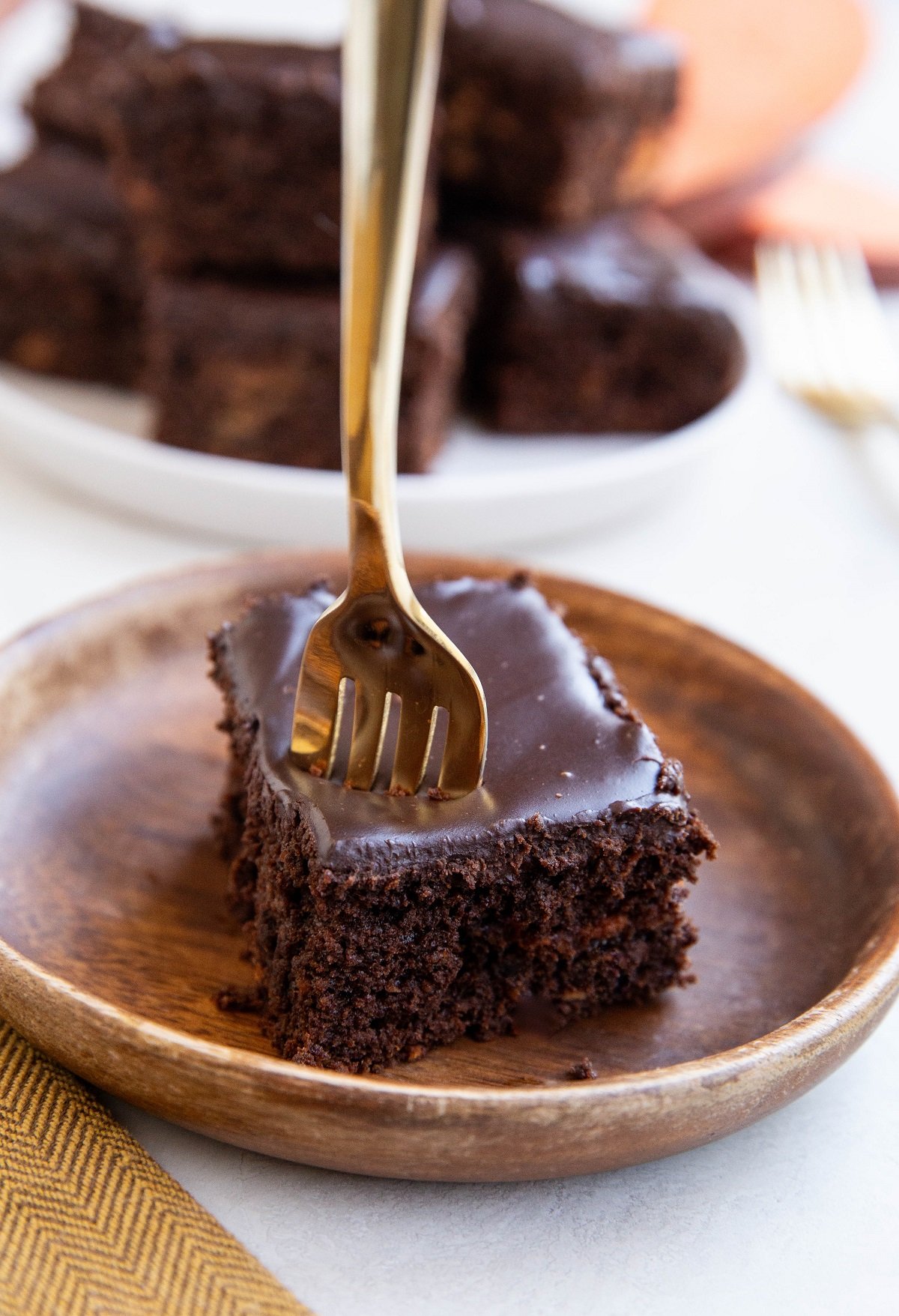 Slice of chocolate cake on a plate with a gold fork about to take a bite.