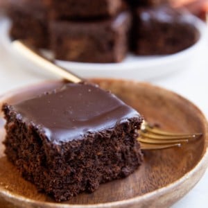 Sweet potato chocolate cake on a wood plate with a plate of chocolate cake in the background.