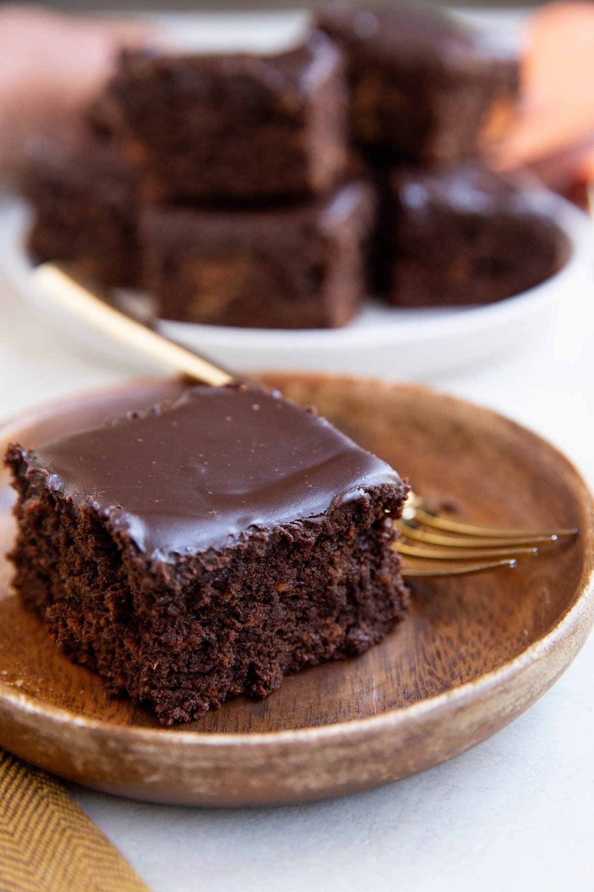 Sweet potato chocolate cake on a wood plate with a plate of chocolate cake in the background.