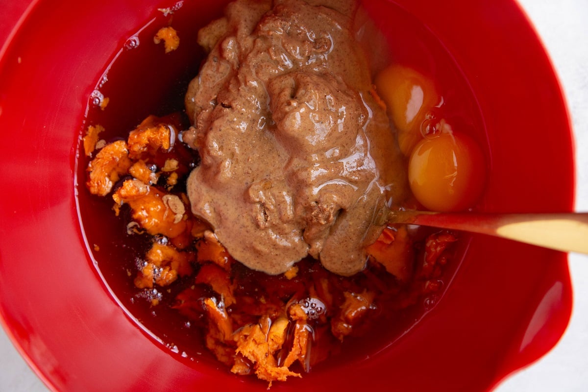 Wet ingredients for sweet potato chocolate cake in a red mixing bowl, ready to be mixed up.