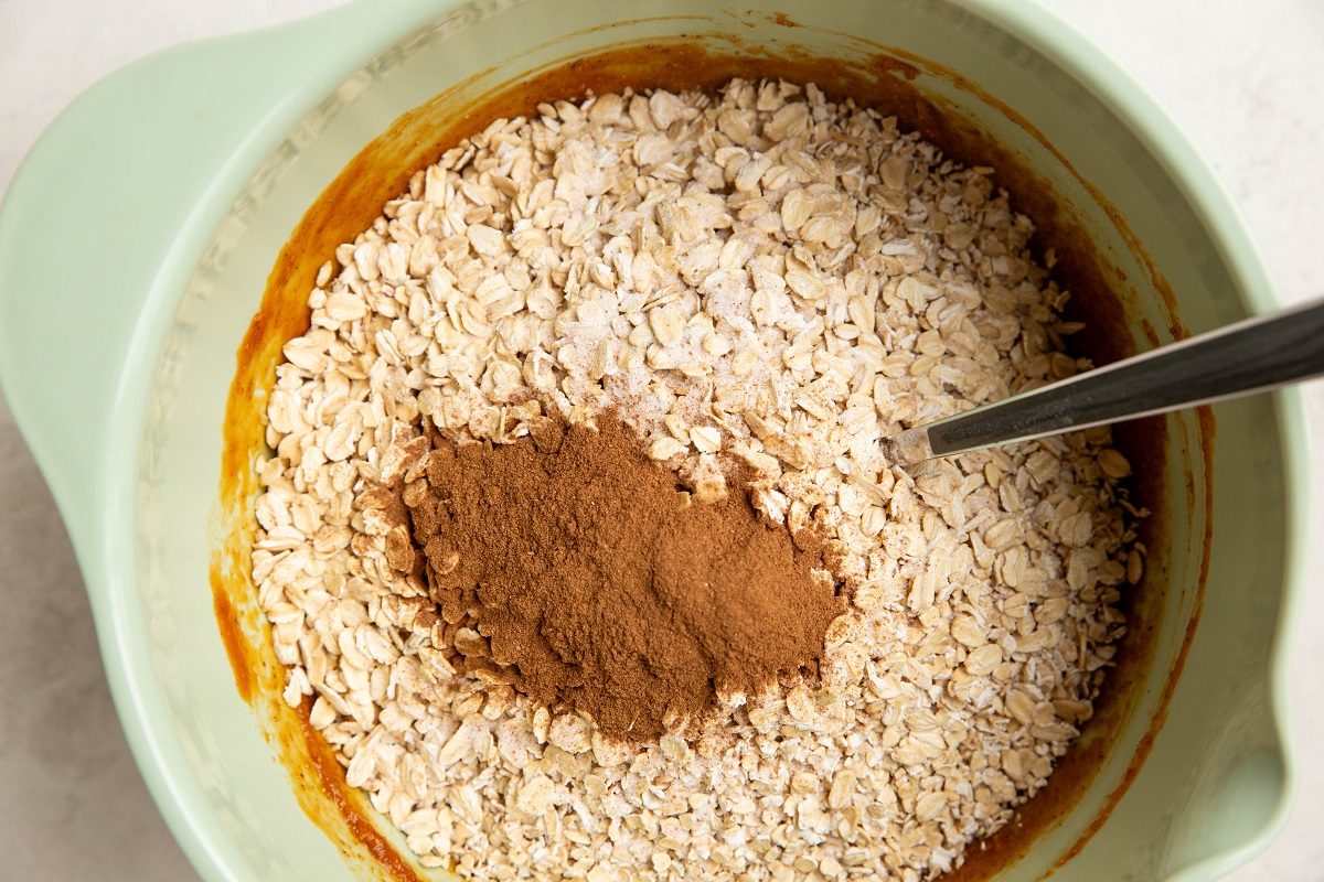 Oats, cinnamon and salt on top of wet ingredients in a mixing bowl to make no-bake oatmeal cups.