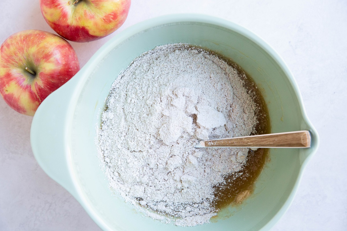 Dry ingredients on top of wet ingredients in a mixing bowl to be mixed into apple bread.