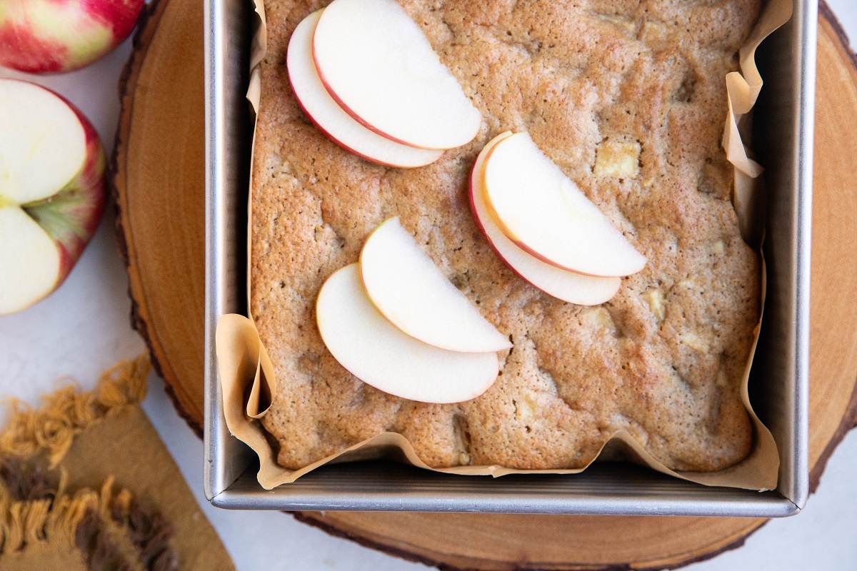 Finished apple cake in a square baking pan with sliced apples on top.