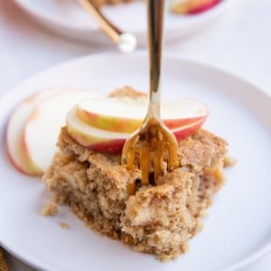 Slice of apple cake on a white plate with a fork taking a bite.