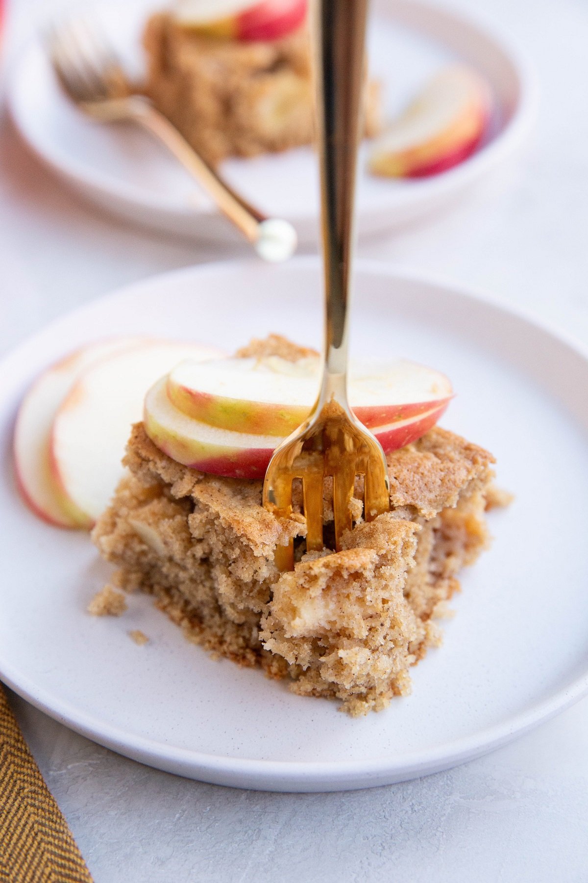 Slice of apple cake on a white plate with a fork taking a bite.