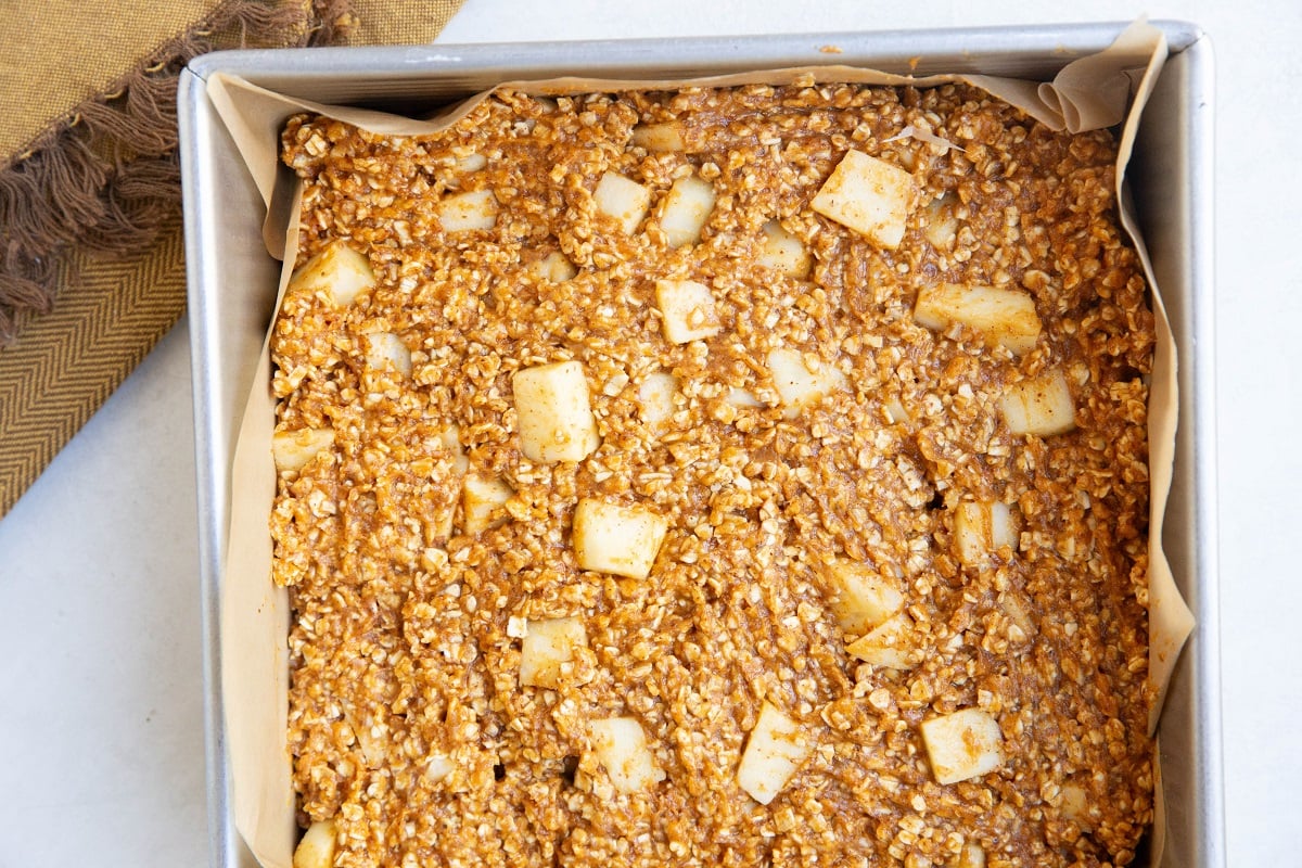 Baking pan lined with parchment paper with apple pumpkin oatmeal mixture inside, ready to bake.