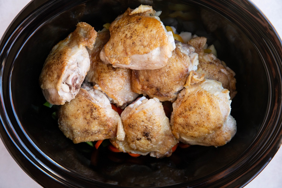 Chicken thighs on top of vegetables in a slow cooker.