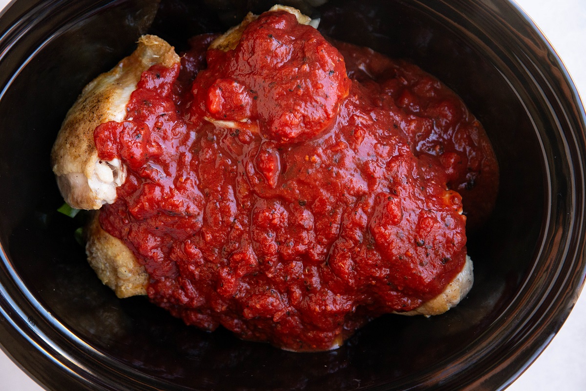 Tomato sauce on top of chicken and vegetables in a crock pot to make chicken cacciatore.