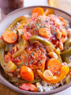 Big bowl of chicken cacciatore over brown rice with white white in the background.