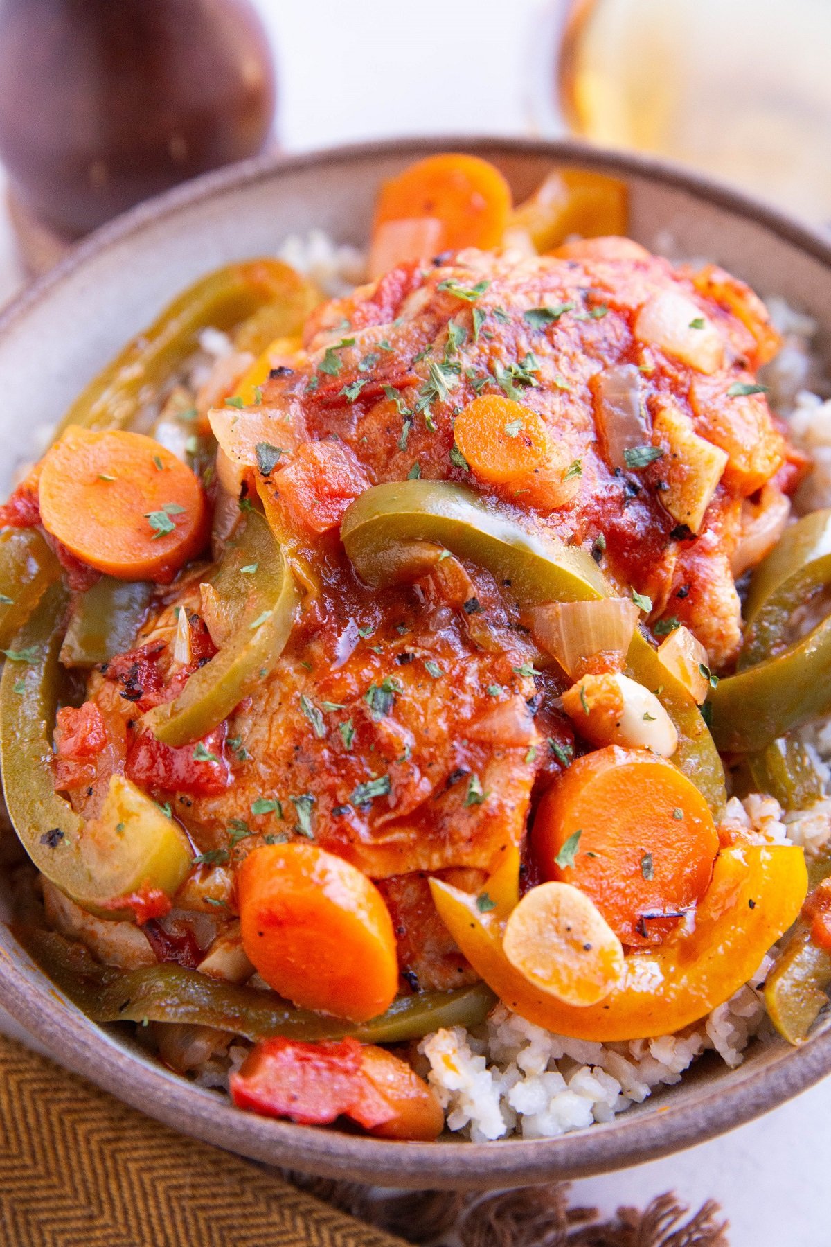 Big bowl of chicken cacciatore over brown rice with white white in the background.