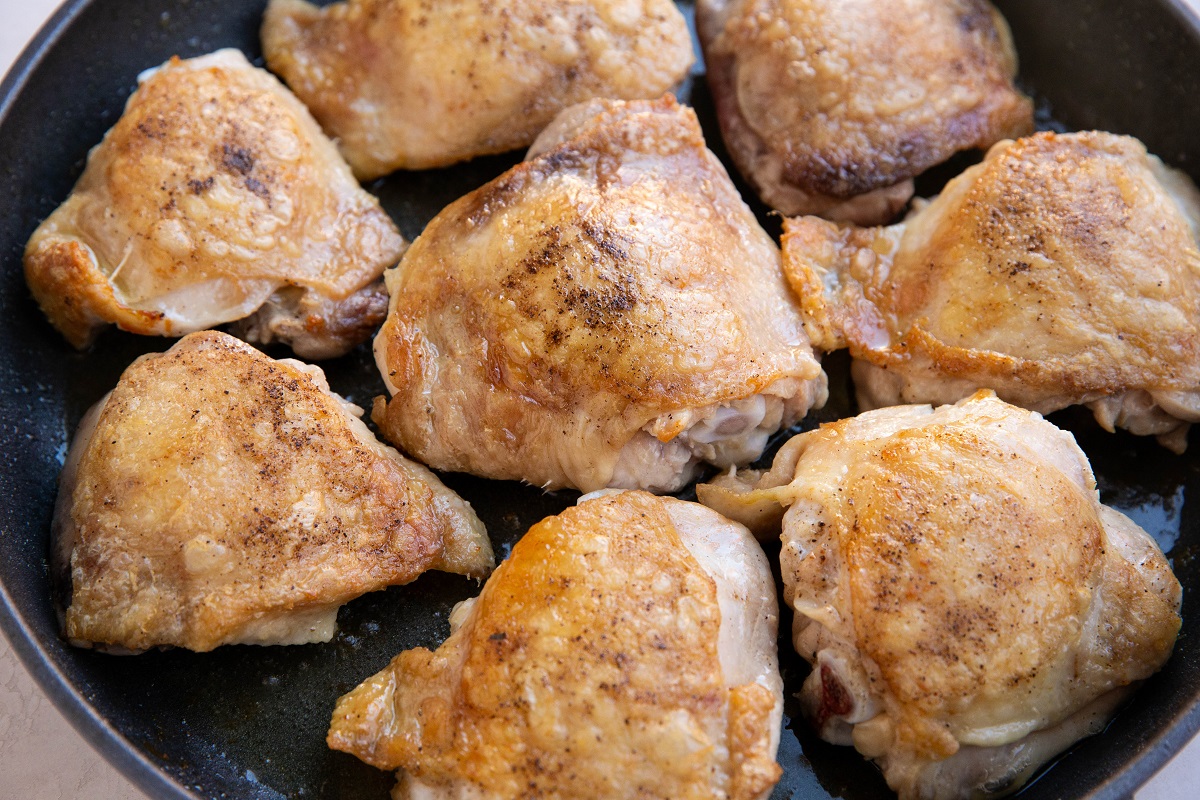skin-on chicken thighs searing in a large skillet.