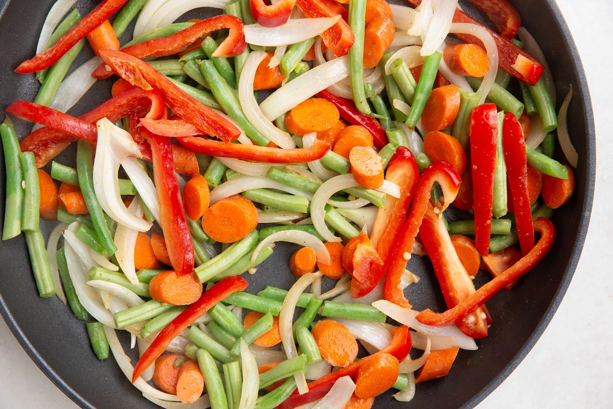 Onion, bell pepper, carrots, and green beans cooking in a skillet.