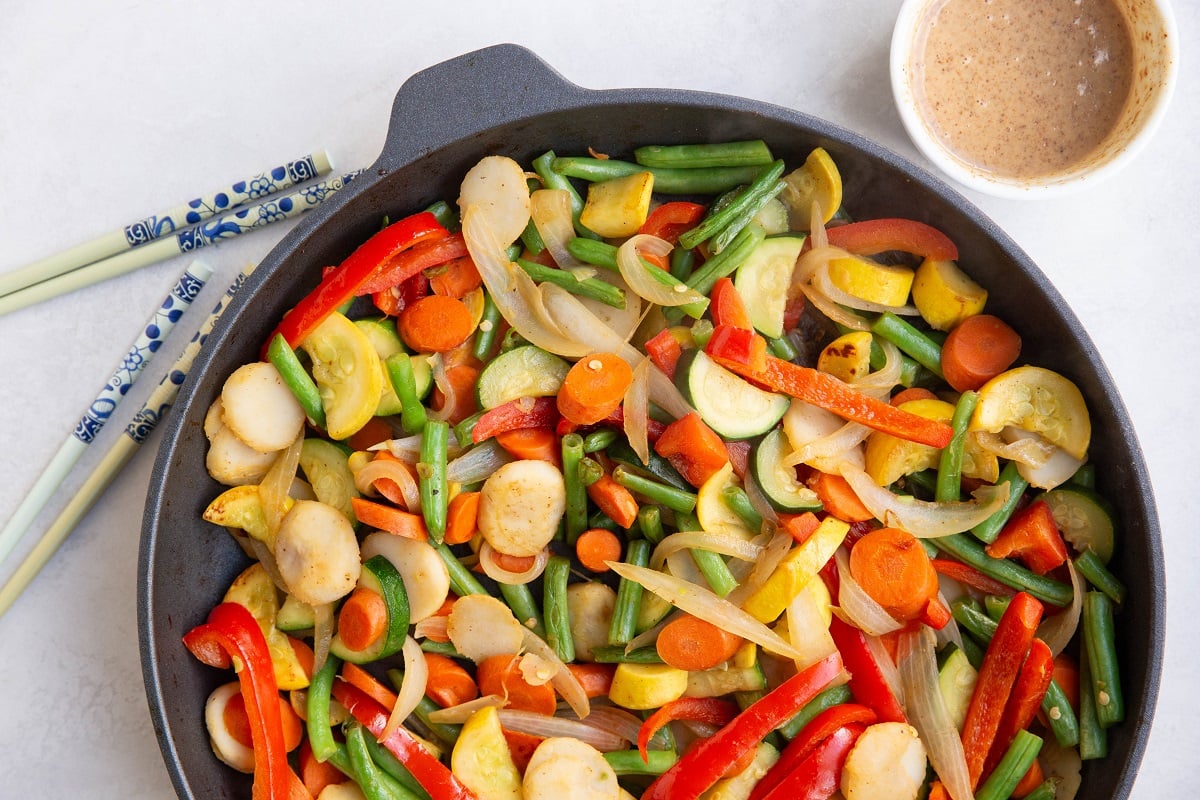 large skillet of stir fry vegetables and sauce and chopsticks to the side.