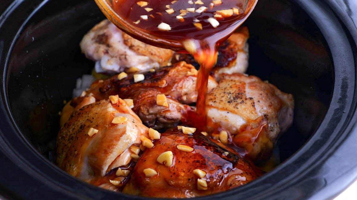 Pouring sauce into the crock pot with the chicken thighs.
