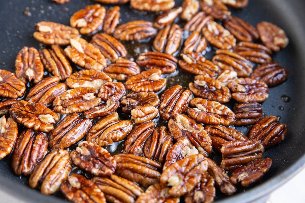 Pecans toasting in pure maple syrup and avocado oil in a skillet, in the process of candying.