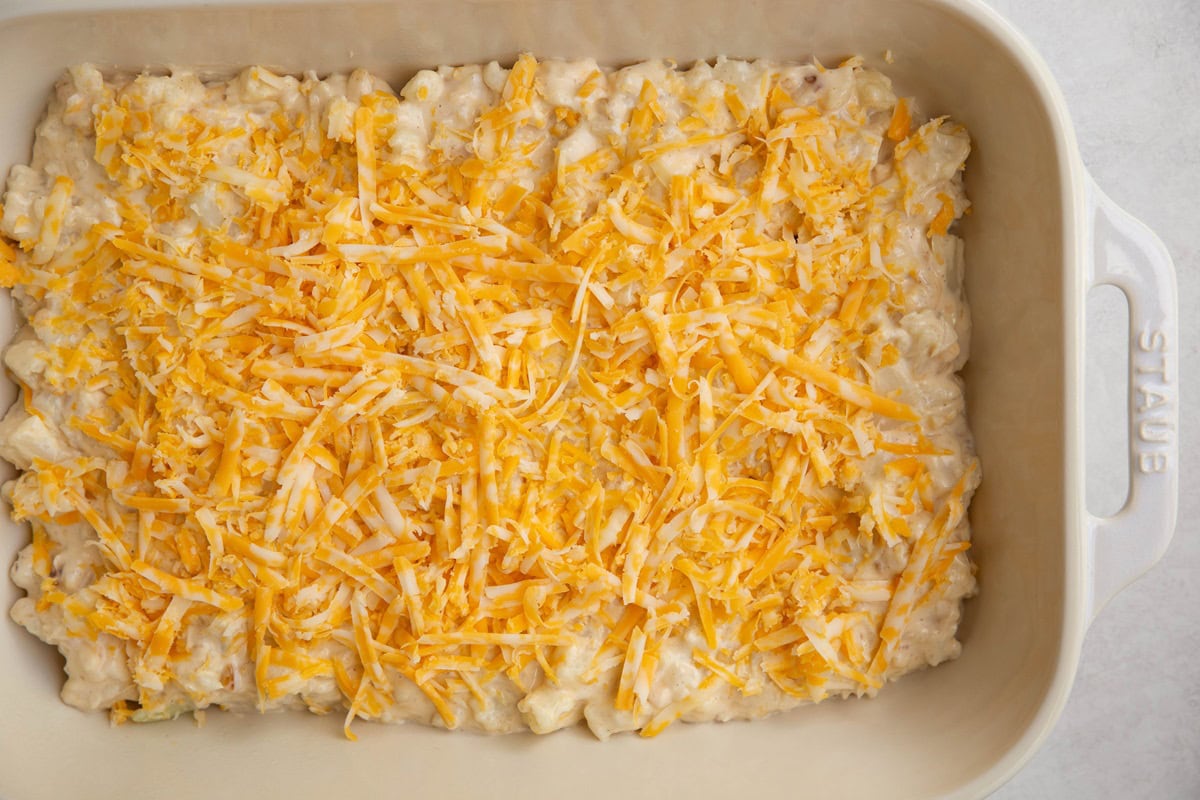 Casserole dish full of cauliflower mac and cheese with cheese sprinkled on top, ready to bake.