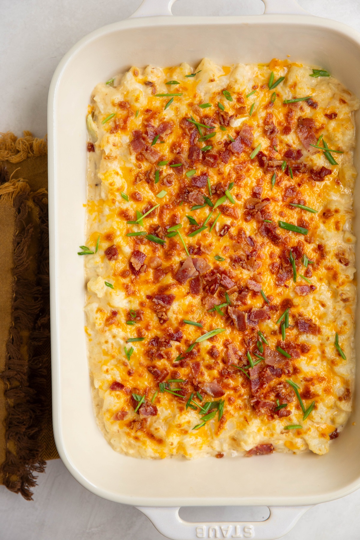 Casserole dish of baked cauliflower mac and cheese with chives and bacon sprinkled on top.