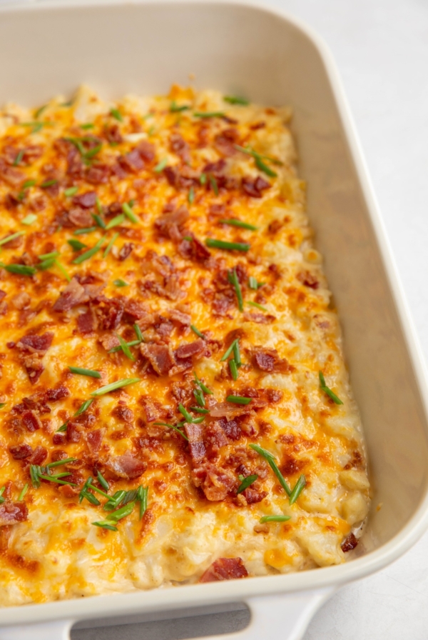 White casserole dish with baked creamy cheesy cauliflower sprinkled with bacon and chives.
