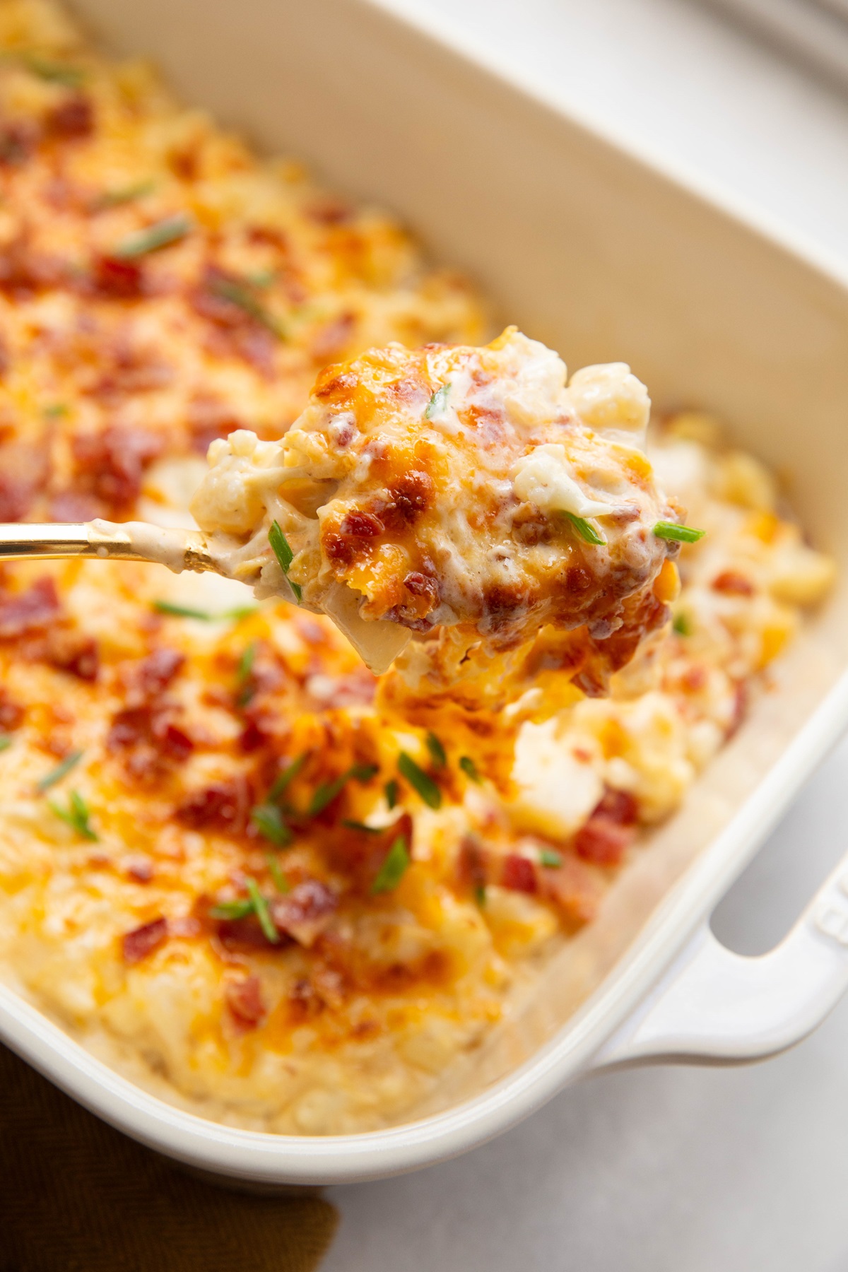 Spoon scooping cauliflower mac and cheese out of a casserole dish.