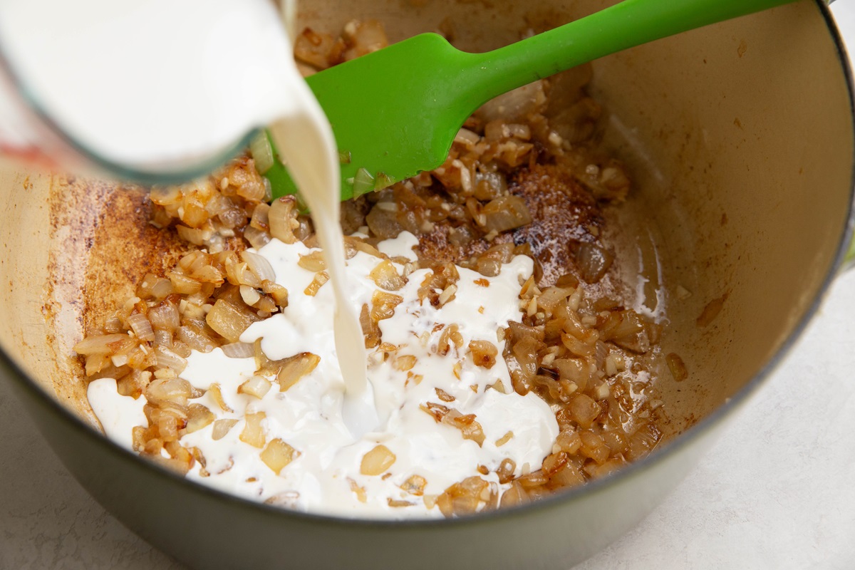 Pouring cream into a large pot with caramelized onions.